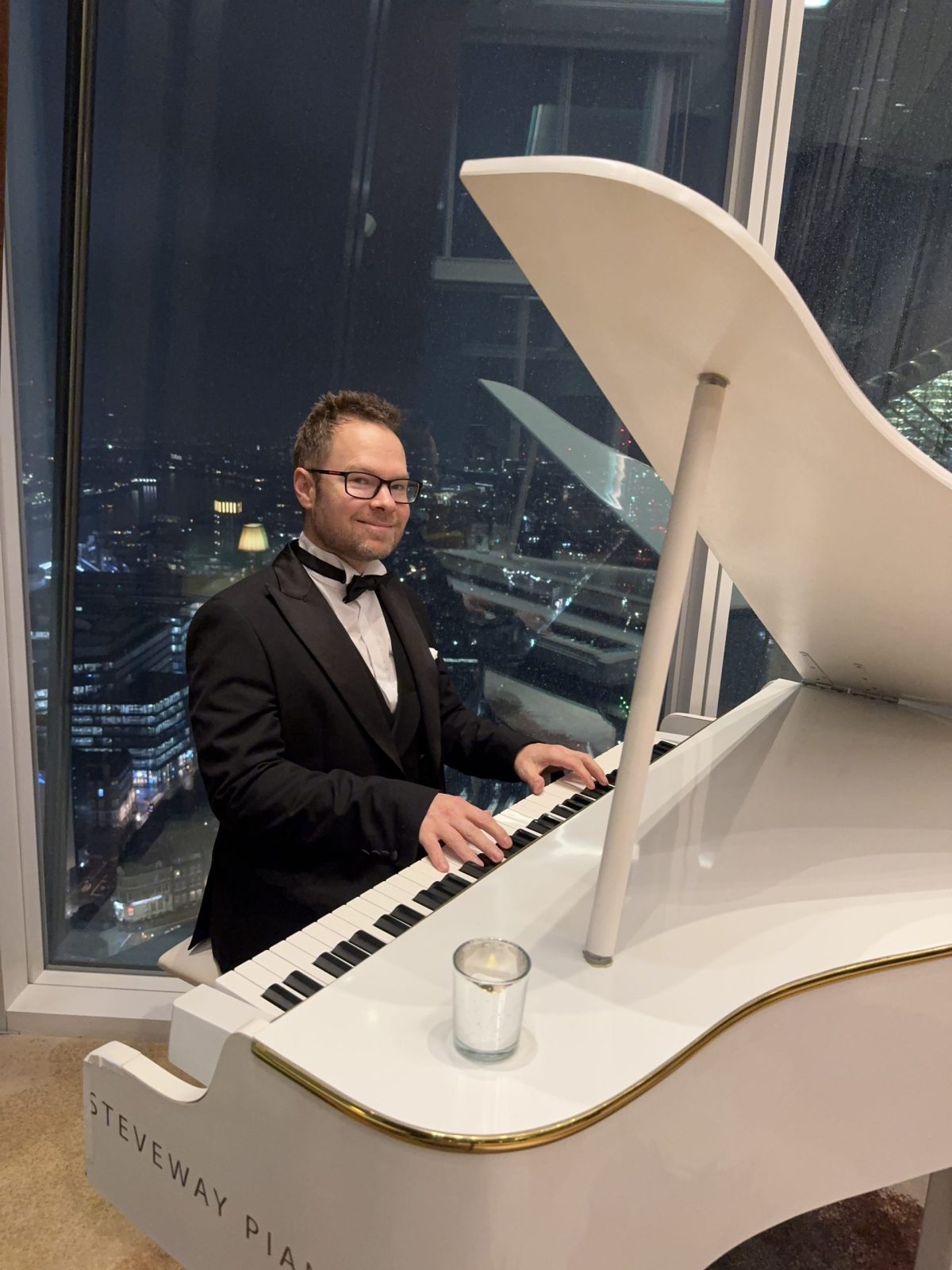 Simon Galfe playing a white grand piano at The Shard, London, at night